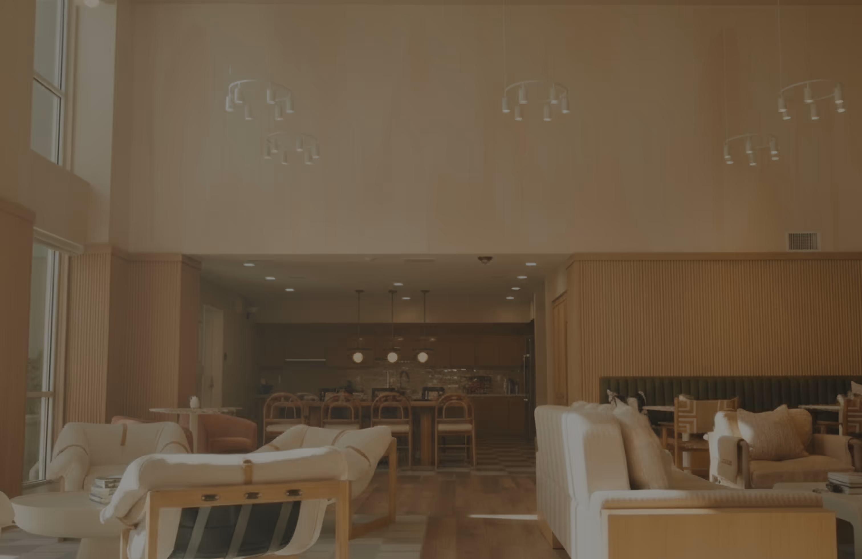 Modern living room with white sofas, wooden chairs, and a dining area with hanging pendant lights.