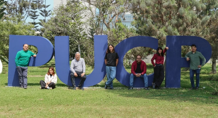 Equipo de la Oficina de Iniciativas Estudiantiles de la PUCP posando frente a las letras monumentales de la universidad en el campus.
