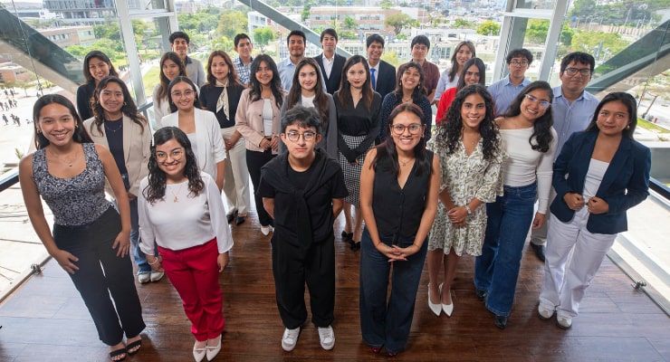 Grupo numeroso de jóvenes posando juntos en un espacio moderno con vista panorámica del campus universitario