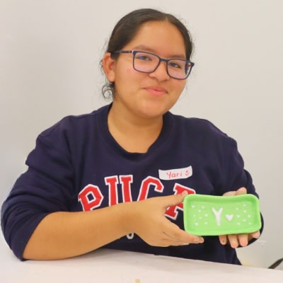 Estudiante sostiene una caja decorada, participando en una actividad de integración o taller.