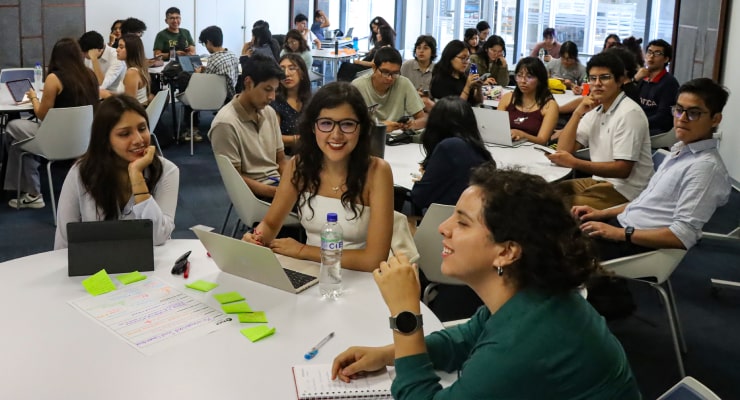 Grupo de estudiantes participa en una dinámica grupal en un aula amplia, conversando y tomando notas durante un taller académico.