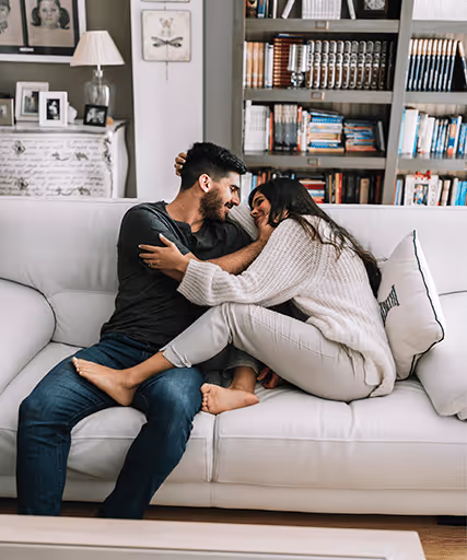 A smiling couple sitting on the couch talking about intimacy and connection with PT-141 therapy