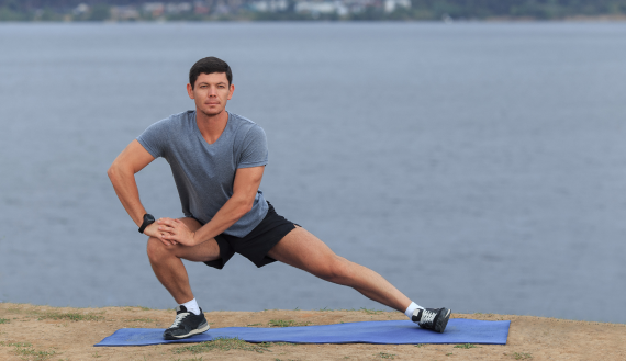 Man stretching on a mat by the lake, improving flexibility and recovery with the help of EPAT shockwave therapy