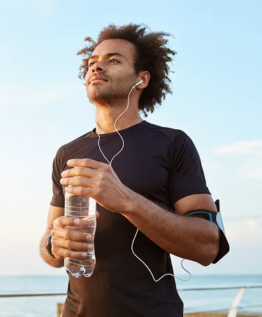 Man holding water bottle and listening to music outdoors post-run, representing immune support and antioxidant benefits from Vitamin C injections.