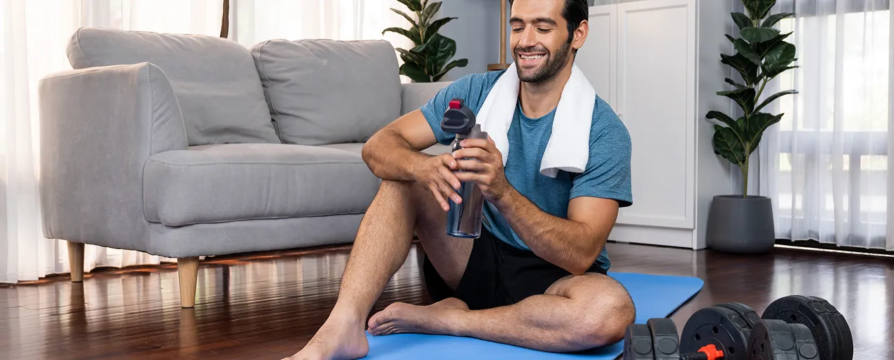 Man relaxing on a yoga mat at home with towel and water bottle, representing post-workout recovery and hydration supported by Vitamin B12 injections.