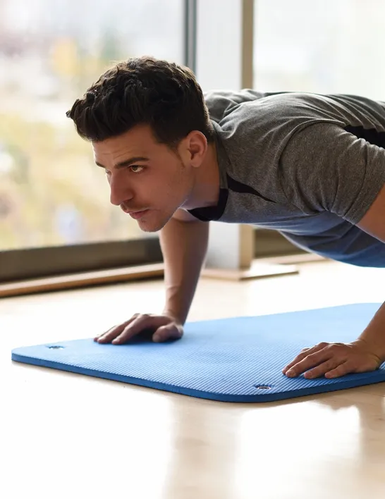 Focused man doing push-ups on a yoga mat indoors, representing increased energy and endurance supported by Vitamin B12 injections