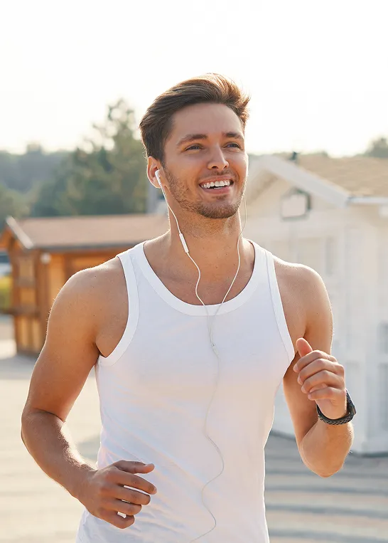 Man jogging outdoors with earbuds and smiling, representing improved energy and mood from Vitamin B12 injections for men.
