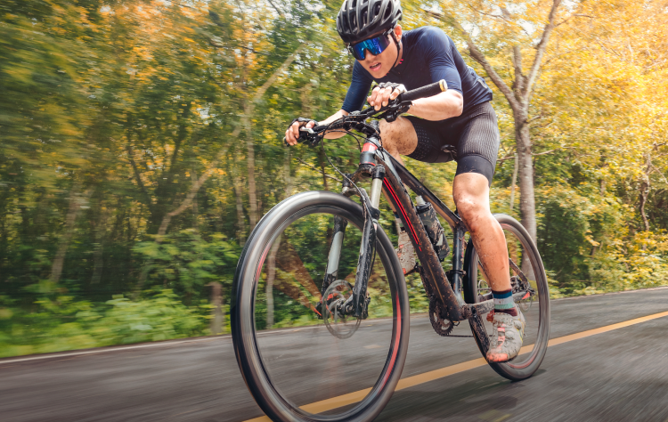 Athletic man cycling on a road through a forest, wearing a helmet and sunglasses, focused on speed and performance.