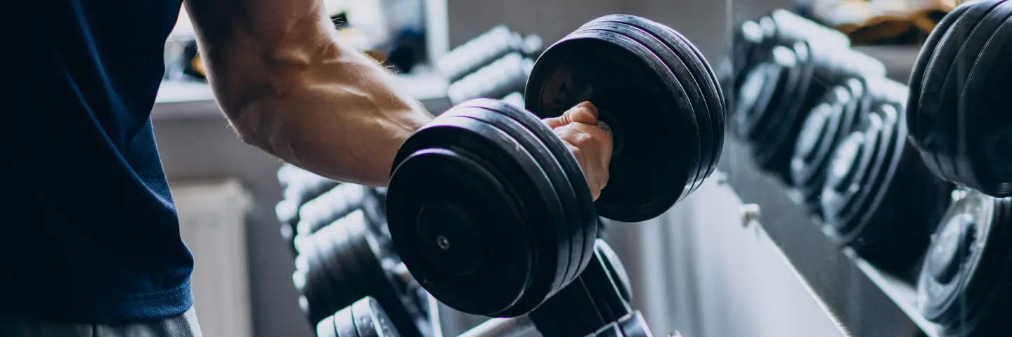 Close-up of a man lifting a heavy dumbbell in a gym, with rows of weights reflected in the mirror.