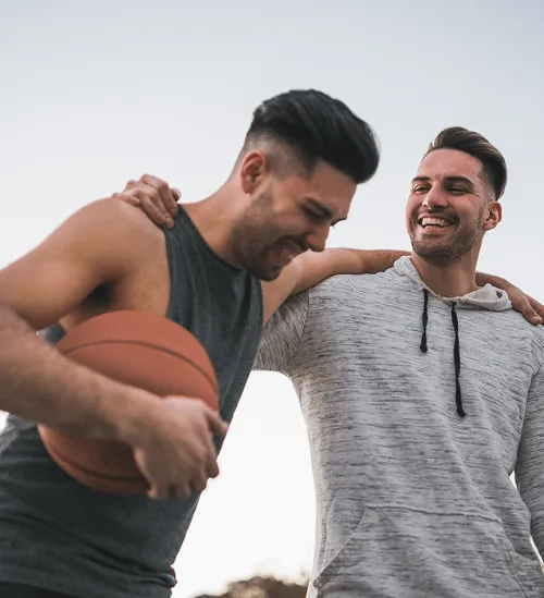 Two men smiling and enjoying time together outdoors, one holding a basketball, representing confidence and enhanced performance after P-Shot treatment at Gameday Men’s Health.