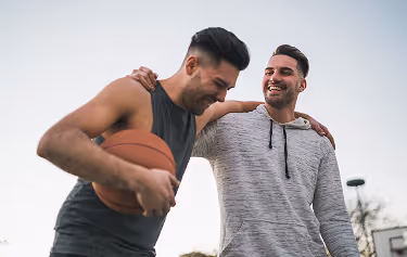Two men smiling and enjoying time together outdoors, one holding a basketball, representing confidence and enhanced performance after P-Shot treatment at Gameday Men’s Health.