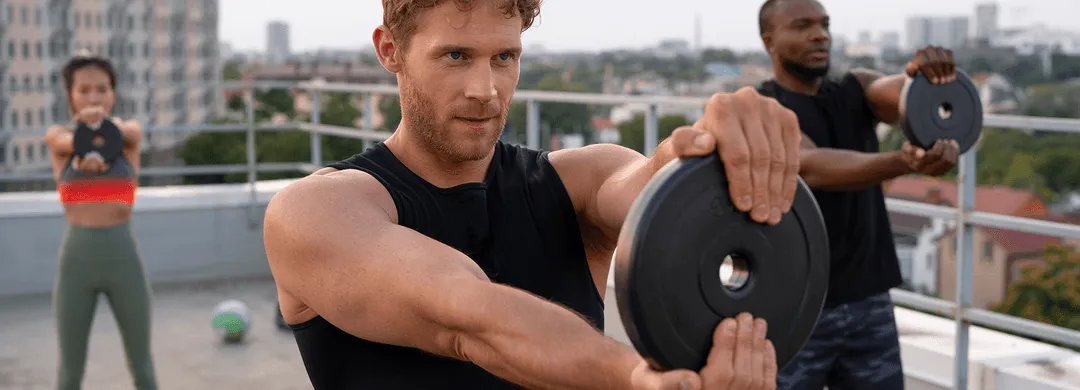 Group of fit individuals performing strength training exercises with weight plates on a rooftop, emphasizing active lifestyles and peak physical performance.