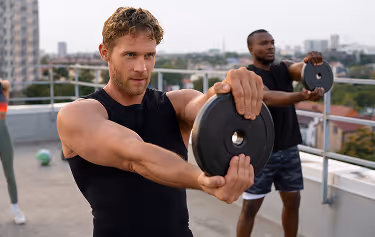 Group of fit individuals performing strength training exercises with weight plates on a rooftop, emphasizing active lifestyles and peak physical performance.