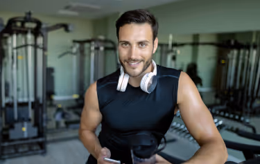 Confident man in athletic wear holding a shaker bottle and phone at the gym, representing improved vitality after GAINSWave® therapy.