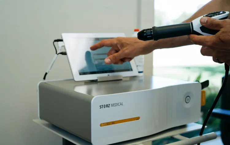 Close-up of a GAINSWave® shockwave therapy device and touchscreen interface used for non-invasive male performance treatments.