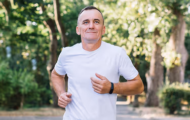 Middle-aged man jogging through a park, representing improved vitality and energy from oral testosterone therapy.