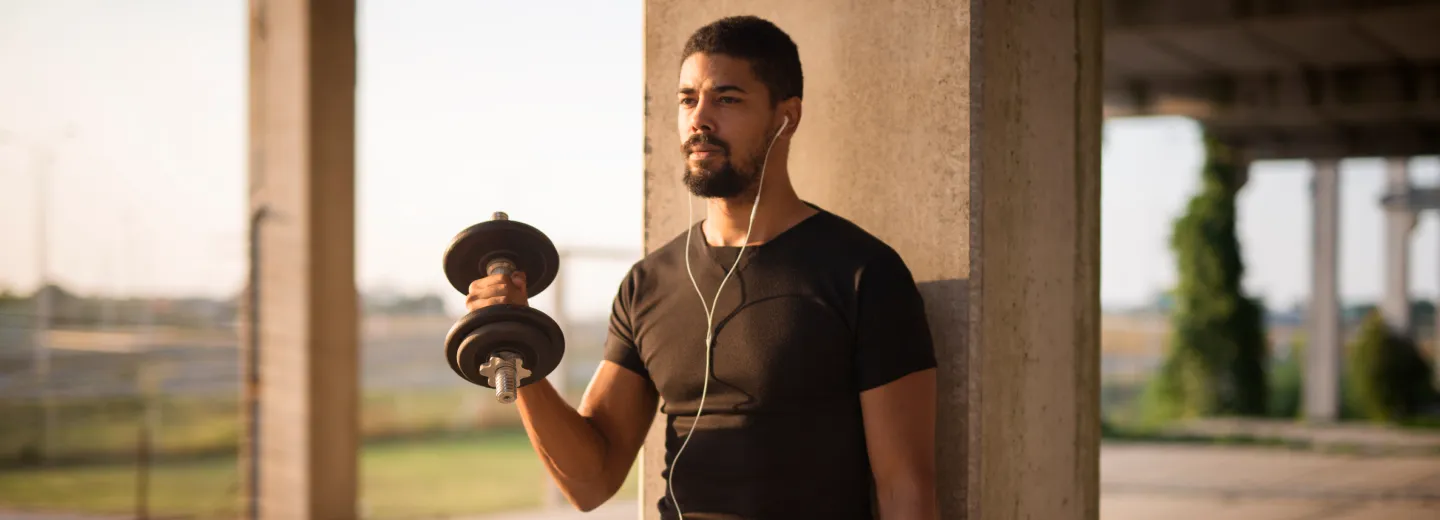 Fit man lifting a dumbbell outdoors while listening to music, representing increased strength and performance with GHRH therapy