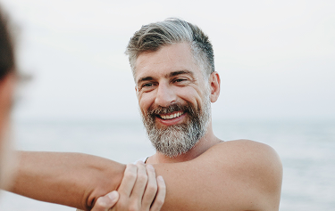 Smiling middle-aged man stretching by the beach, representing improved flexibility and vitality with Sermorelin therapy
