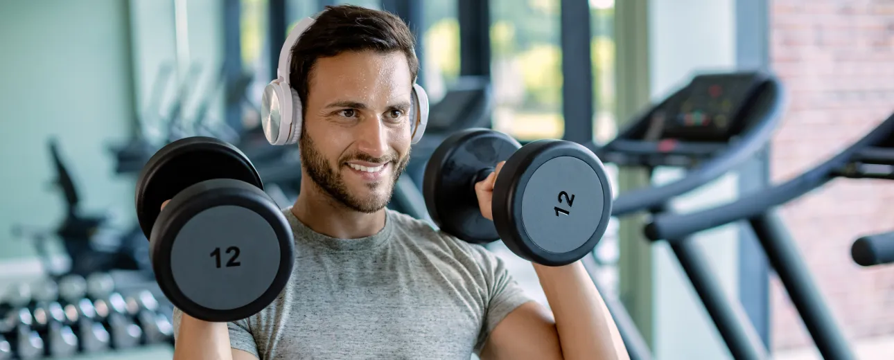 Man lifting dumbbells at the gym while listening to music, representing increased energy and fat-burning support with MIC lipotropic injections.