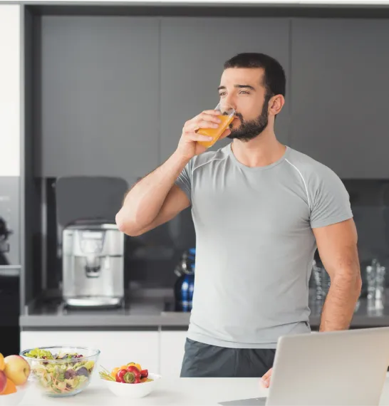 Man drinking juice in a modern kitchen with healthy food on the counter, representing clean eating and metabolic support from MIC lipotropic injections