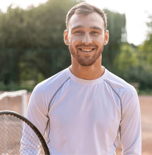 Smiling man holding a tennis racket on the court, reflecting the immune support and antioxidant benefits of Vitamin C injections for active men.