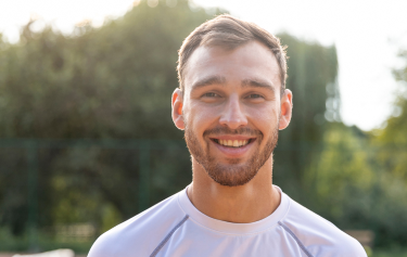 Smiling man holding a tennis racket on the court, reflecting the immune support and antioxidant benefits of Vitamin C injections for active men.