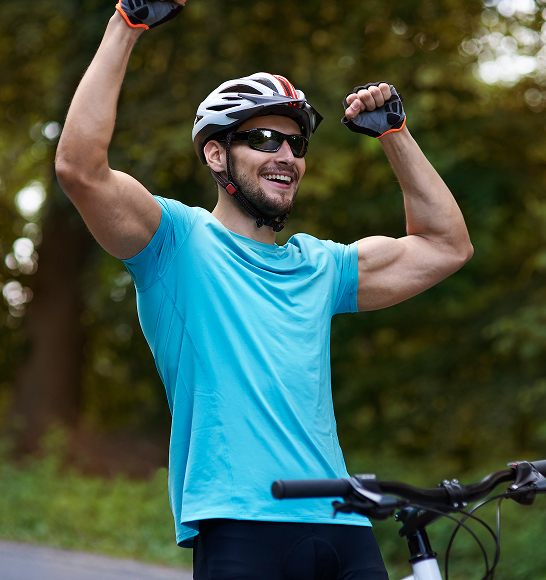 Energetic man celebrating post-bike ride with arms raised, highlighting the detoxification, immune support, and cellular recovery benefits of glutathione injections.