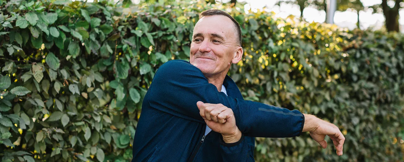 Older man stretching outdoors with a smile, representing joint flexibility, energy, and wellness benefits supported by vitamin injections.