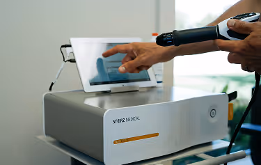 Close-up of a GAINSWave® shockwave therapy device and touchscreen interface used for non-invasive male performance treatments.