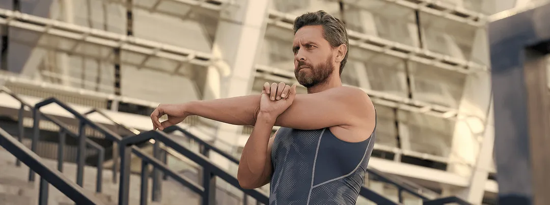 Man stretching near modern stadium steps, representing strength and mobility with support from GHRH peptide therapy