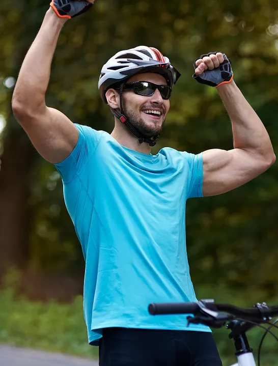 Fit man wearing a helmet and sunglasses raising his arms in victory next to a bicycle, representing confidence, vitality, and the impact of testosterone therapy.