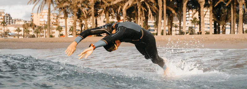 Man in a wetsuit diving into the ocean near a tropical beach, symbolizing energy, vitality, and active lifestyle benefits of testosterone therapy.