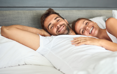 Happy couple relaxing in bed, symbolizing improved energy and intimacy from oral testosterone therapy.
