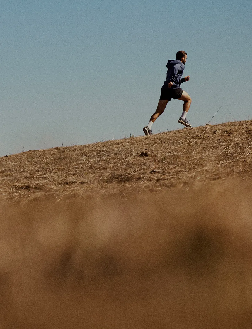 Runner training hard on a hillside during early morning light, embodying the physical transformation and confidence men gain through Gameday treatments.
