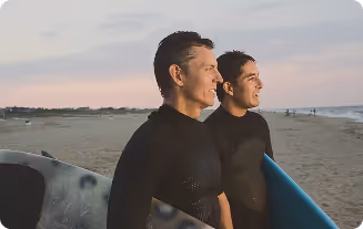 Two men standing with surfboards on the beach, symbolizing boosted energy and performance from vitamins and peptide therapy.