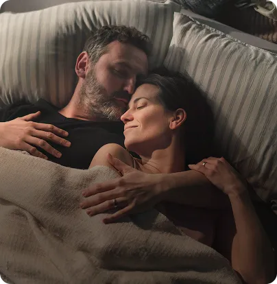 Man and woman relaxing in bed with warm smiles, symbolizing the benefits of addressing sexual wellness and strengthening intimate relationships.