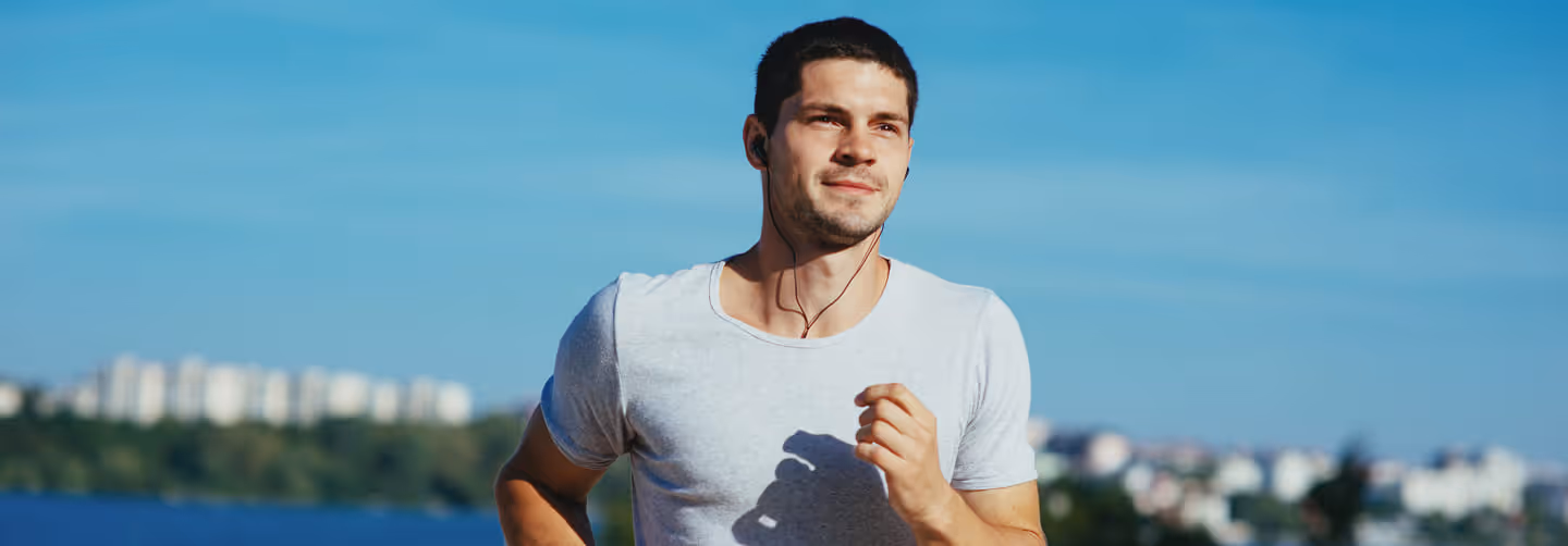 Man running near water with earphones in, reflecting boosted stamina and metabolism support from B vitamin therapy.