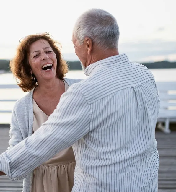 Older couple smiling and dancing outside on a dock.