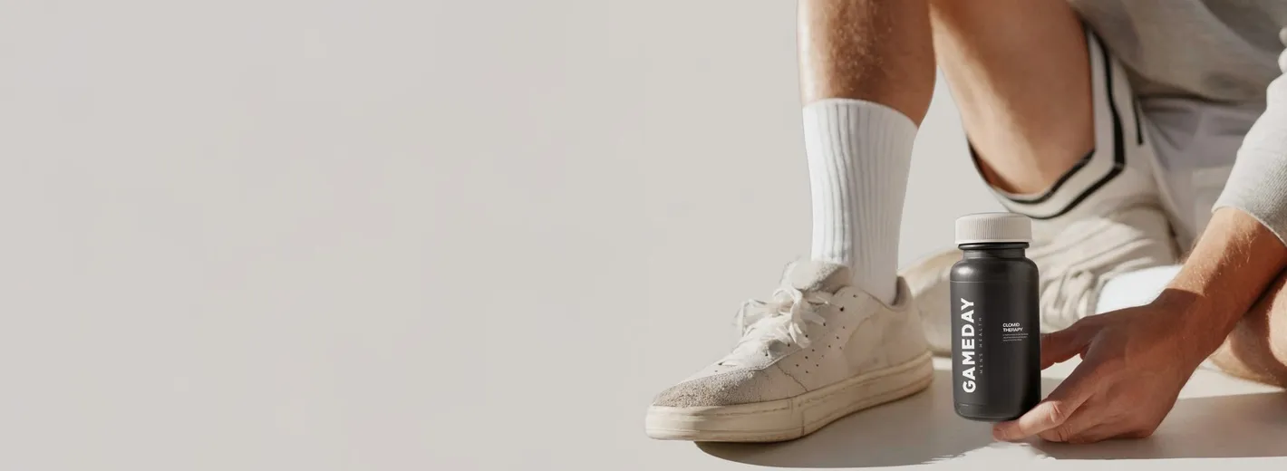 Close up of a man tying athletic shoes while holding a Gameday Men’s Health bottle
