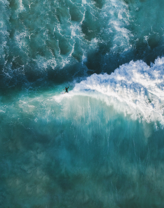 Luftaufnahme eines Surfers, der eine große Welle auf dem blauen Ozean reitet.