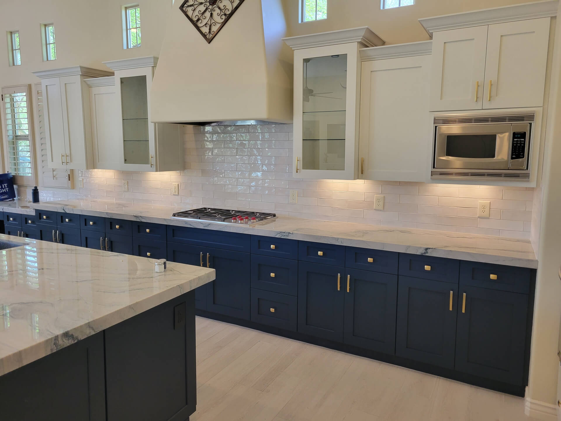 Modern kitchen with navy blue lower cabinets, white upper cabinets, marble countertops, and stainless steel microwave.