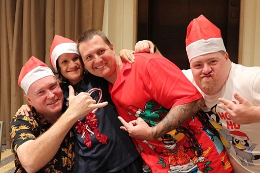 Four people in Christmas hats and festive shirts smiling and posing for a photo at a holiday disco.