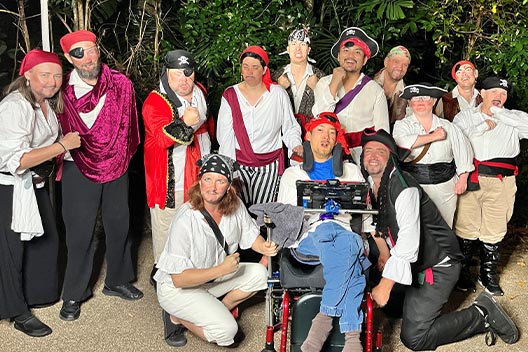 A group of people dressed in various pirate costumes posing together outdoors at night for Shakespeare night
