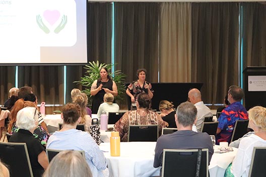Two women presenting on a stage to a seated audience at the Disability Support Worker Conference.