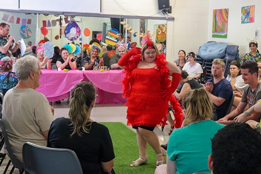 A smiling woman in a red fringed dress and gloves, posing on a green runway at an Easter Bonanza event.