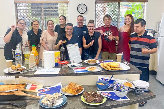 A group of people smiling behind a table filled with diverse international foods for Harmony Day.