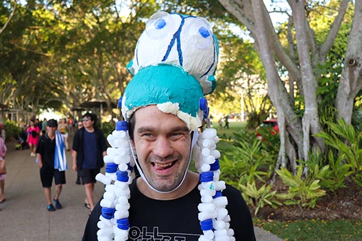 A smiling man at a festival wearing a large, homemade blue and white octopus-like helmet.