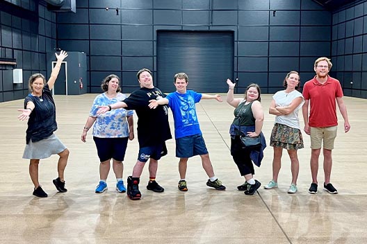 A group of seven people from ARC Creatives posing playfully on a large, empty wooden stage.