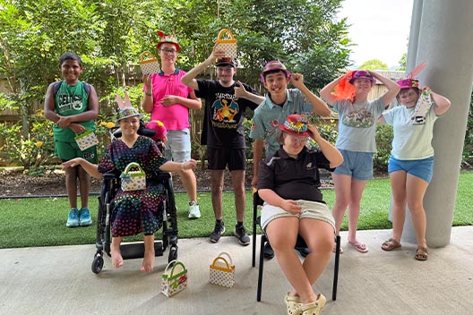 A group of eight young people holding Easter baskets and wearing novelty hats for a School Holiday Program.