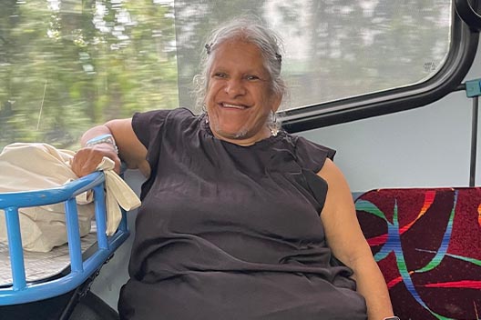 A woman in a dark grey top smiling brightly while seated on a bus.